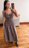 A woman takes a mirror selfie wearing a brown and beige plaid midi dress with ruffled straps and a smocked bodice, standing on a wooden floor in front of a light-colored cabinet.