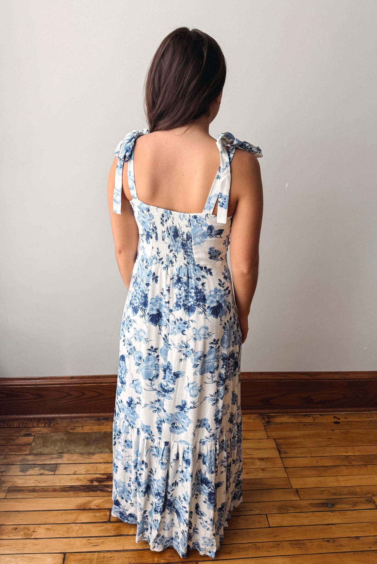 Woman wearing a floral dress standing on a wooden floor with a plain wall background