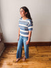Woman wearing a blue and white striped shirt and jeans standing on a wooden floor.