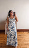 Woman wearing a floral dress taking a mirror selfie in a room with wooden flooring.