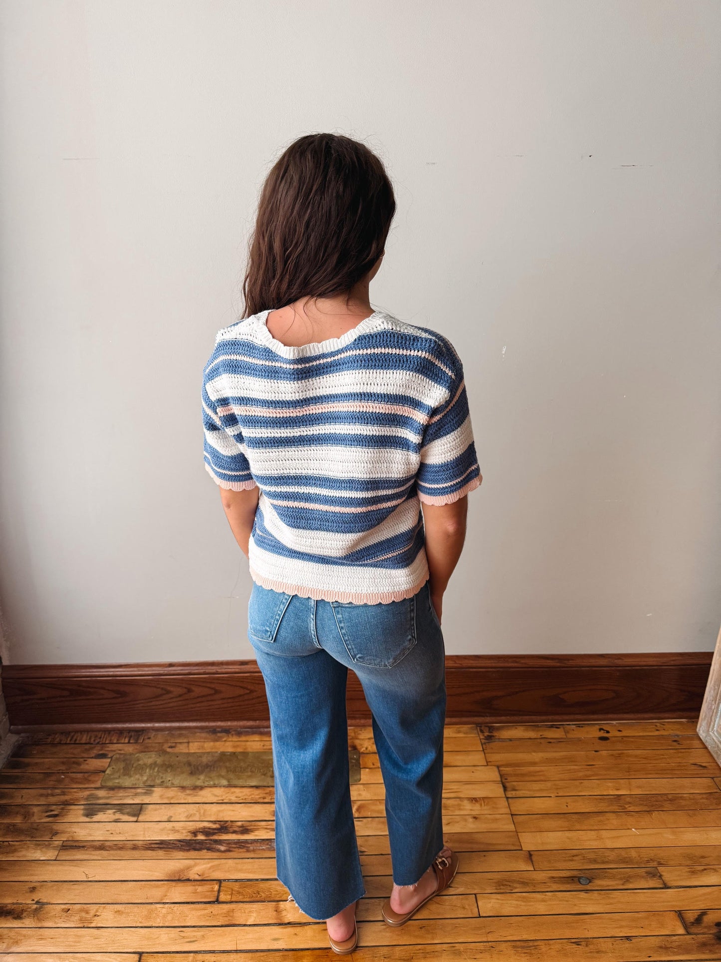 Person wearing a blue and white striped sweater and blue jeans standing in a room with wooden flooring.