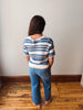 Person wearing a blue and white striped sweater and blue jeans standing in a room with wooden flooring.