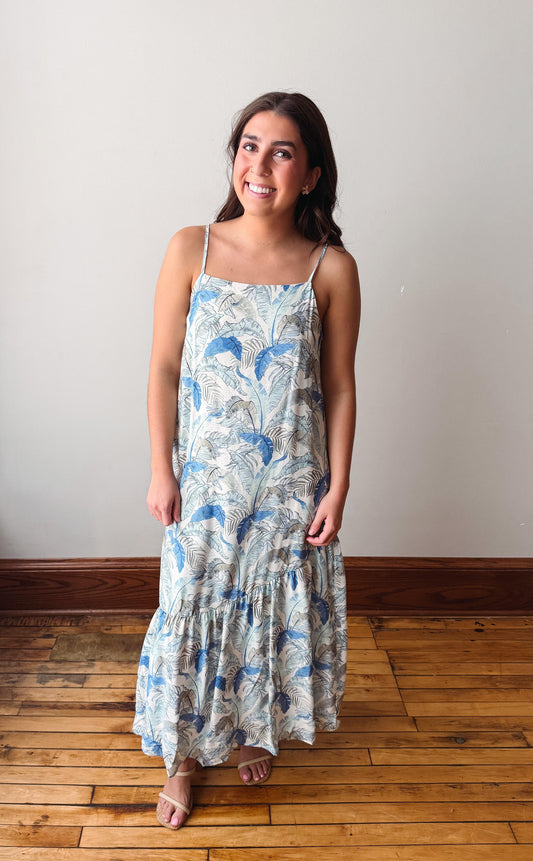 Woman wearing a floral dress standing on a wooden floor with a white wall background