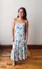 Woman wearing a floral dress standing on a wooden floor with a white wall background