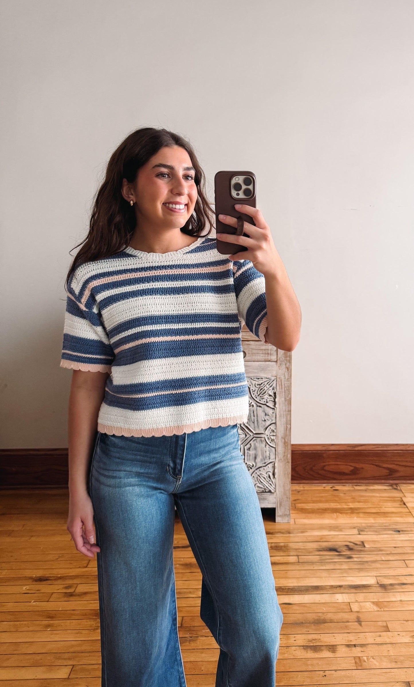 Woman taking a mirror selfie wearing a striped sweater and jeans indoors.