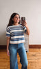 Woman taking a mirror selfie wearing a striped sweater and jeans indoors.