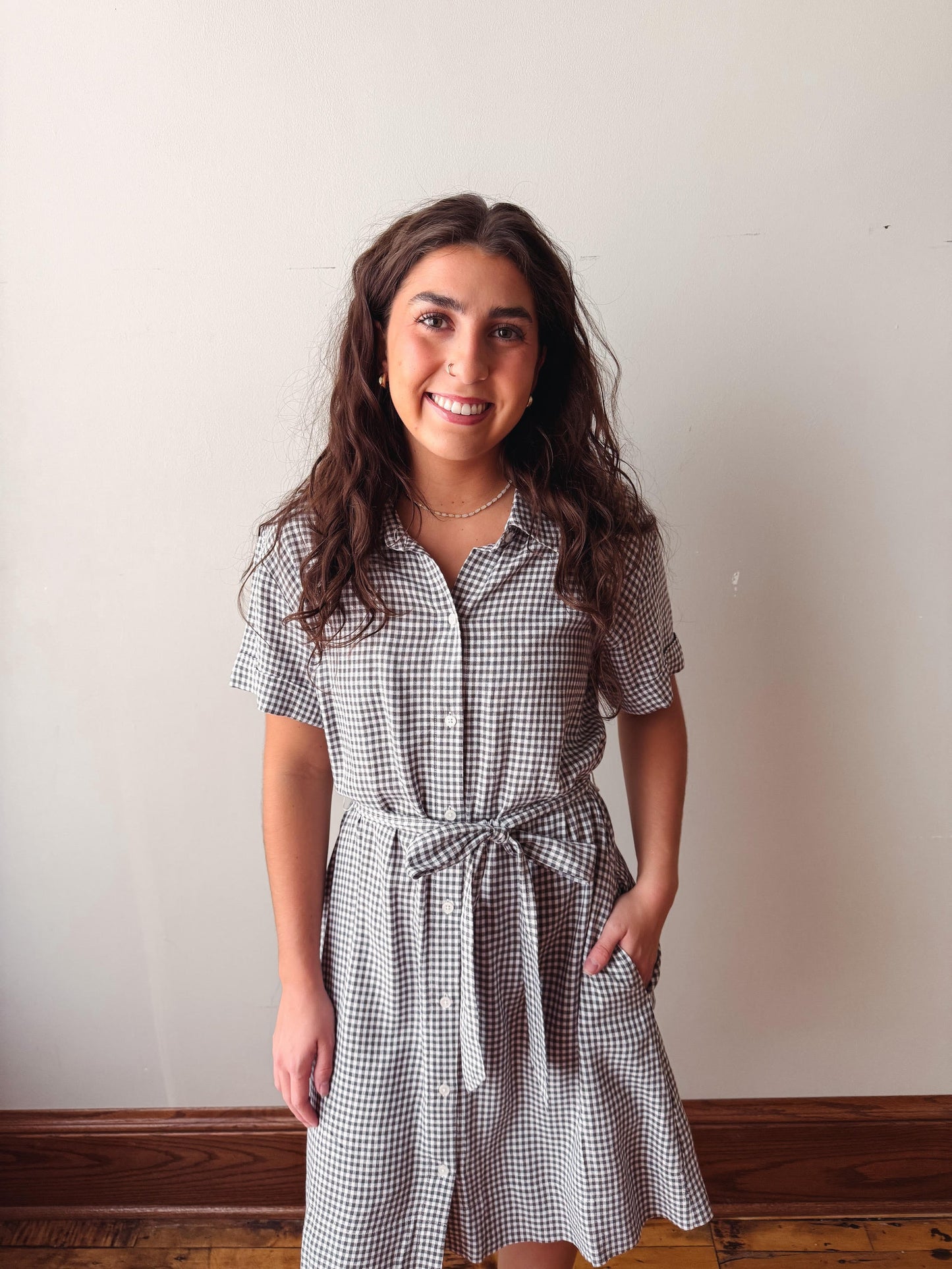 Woman wearing a checkered dress standing against a plain wall.