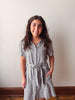 Woman wearing a checkered dress standing against a plain wall.
