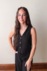 Woman wearing a black sleeveless top with buttons against a plain background