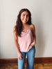 Woman wearing a pink tank top and blue jeans standing against a plain wall.