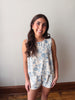 Woman wearing a floral romper against a plain wall.