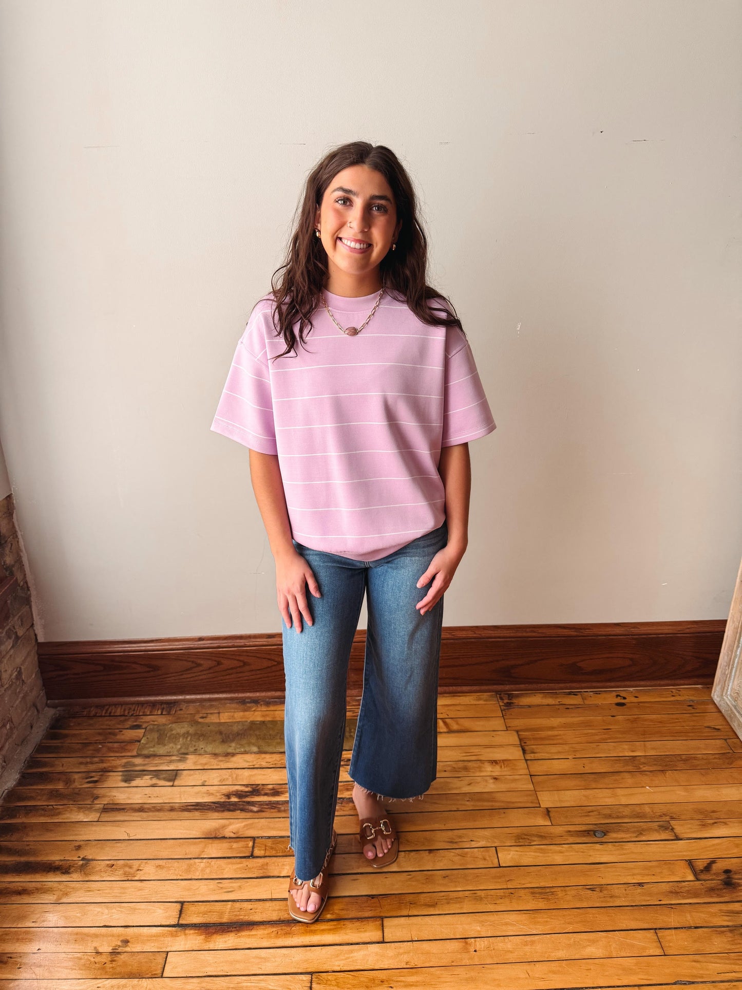 Woman wearing a pink striped shirt and blue jeans standing on a wooden floor.