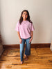 Woman wearing a pink striped shirt and blue jeans standing on a wooden floor.