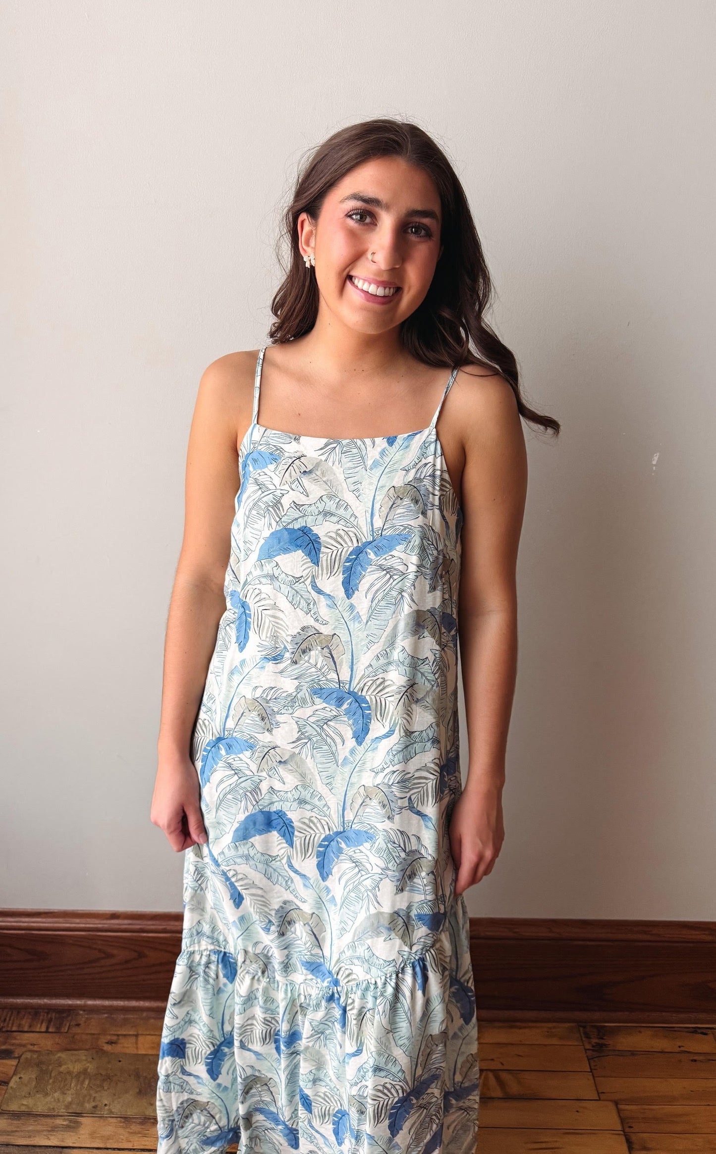 Woman wearing a floral dress standing against a plain wall.