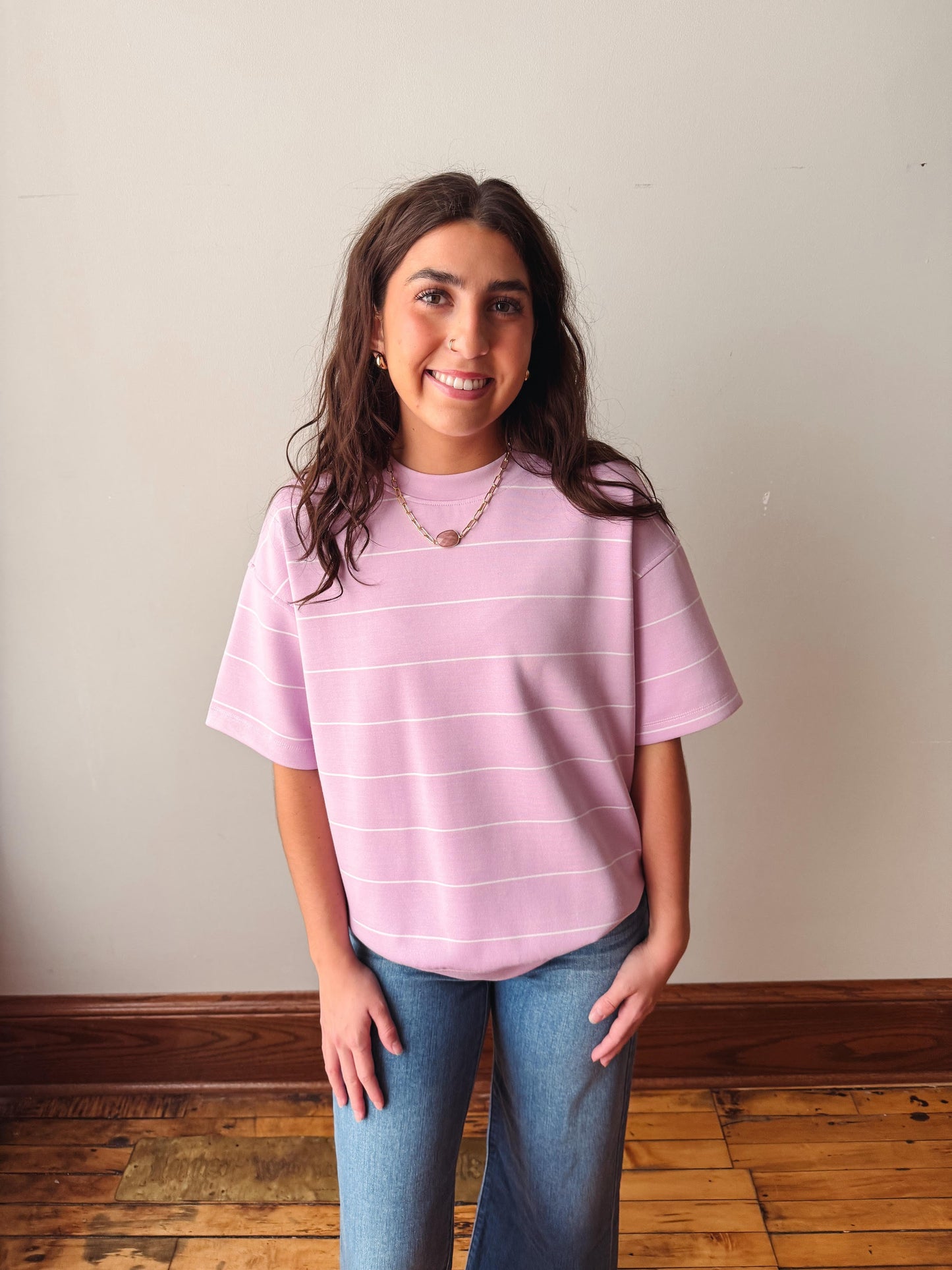 Person wearing a pink striped shirt and blue jeans standing against a plain wall.