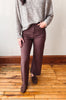 A person wearing brown wide-leg cropped pants, a gray knit sweater, and brown loafers, standing on a wooden floor against a plain wall.