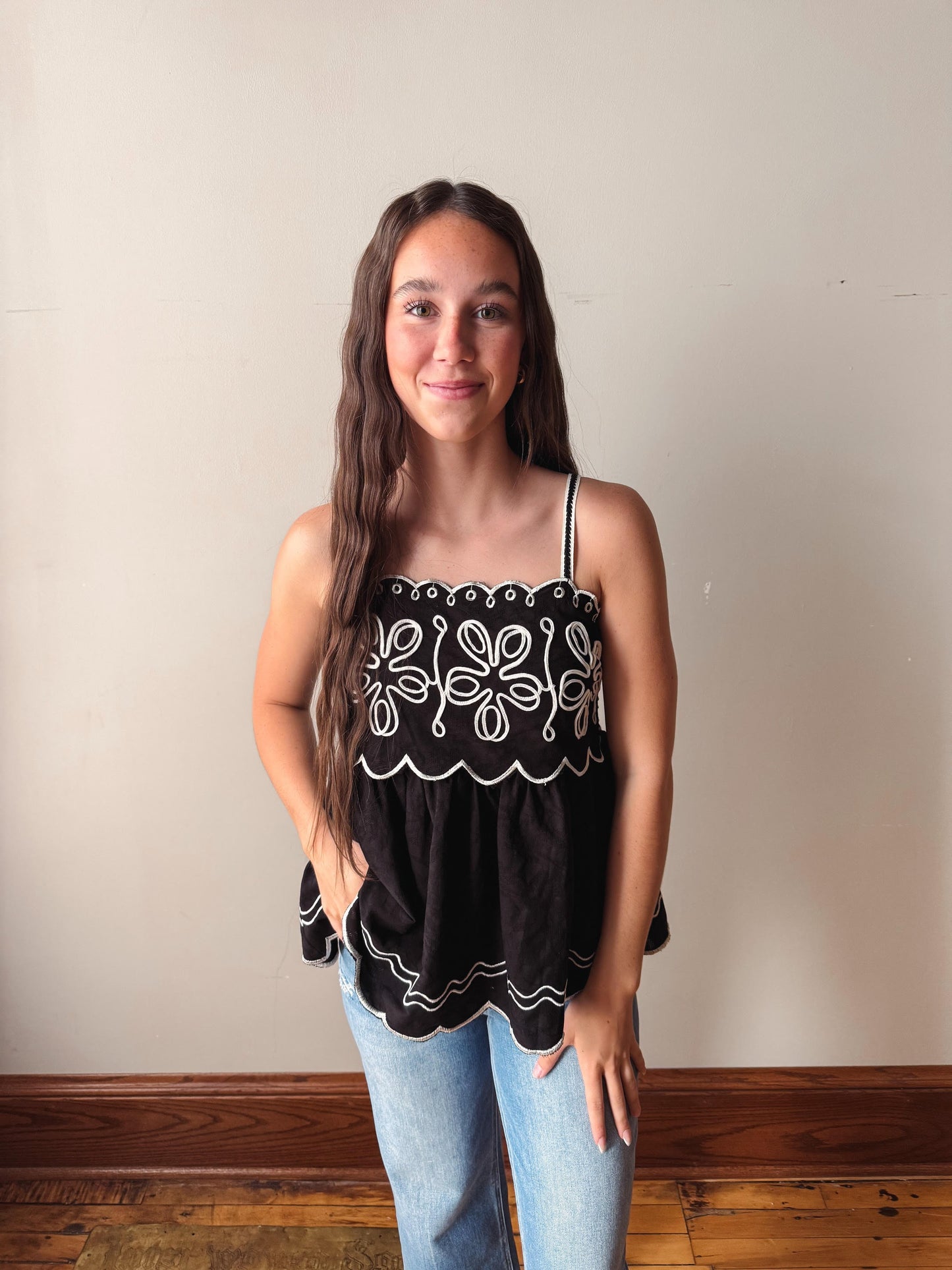 Woman wearing a black top with white patterns against a plain wall.