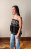 Young girl wearing a black lace top and blue jeans against a plain wall.