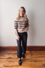 Woman wearing a striped sweater and black pants standing on a wooden floor.