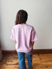 Person wearing a light pink striped shirt and blue jeans standing against a plain wall.