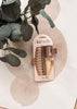 A Kitsch claw clip set in two shades of taupe, packaged on a beige cardboard hanger and styled on a white surface with a beige circular pattern and green eucalyptus leaves.