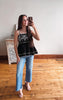 Woman taking a mirror selfie wearing a black top with white lace details and blue jeans.