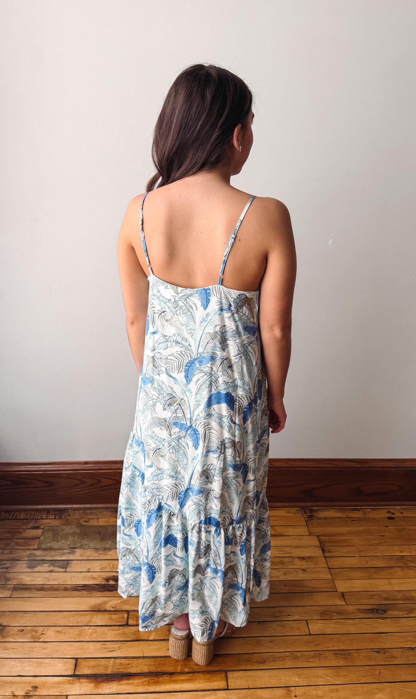 Woman wearing a floral dress standing on a wooden floor with a white wall background