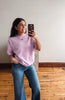 Woman taking a mirror selfie wearing a pink striped shirt and blue jeans in a room with wooden flooring.