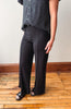 A person wearing black wide-leg pants with a black and white polka dot blouse, standing on a wooden floor against a light wall.