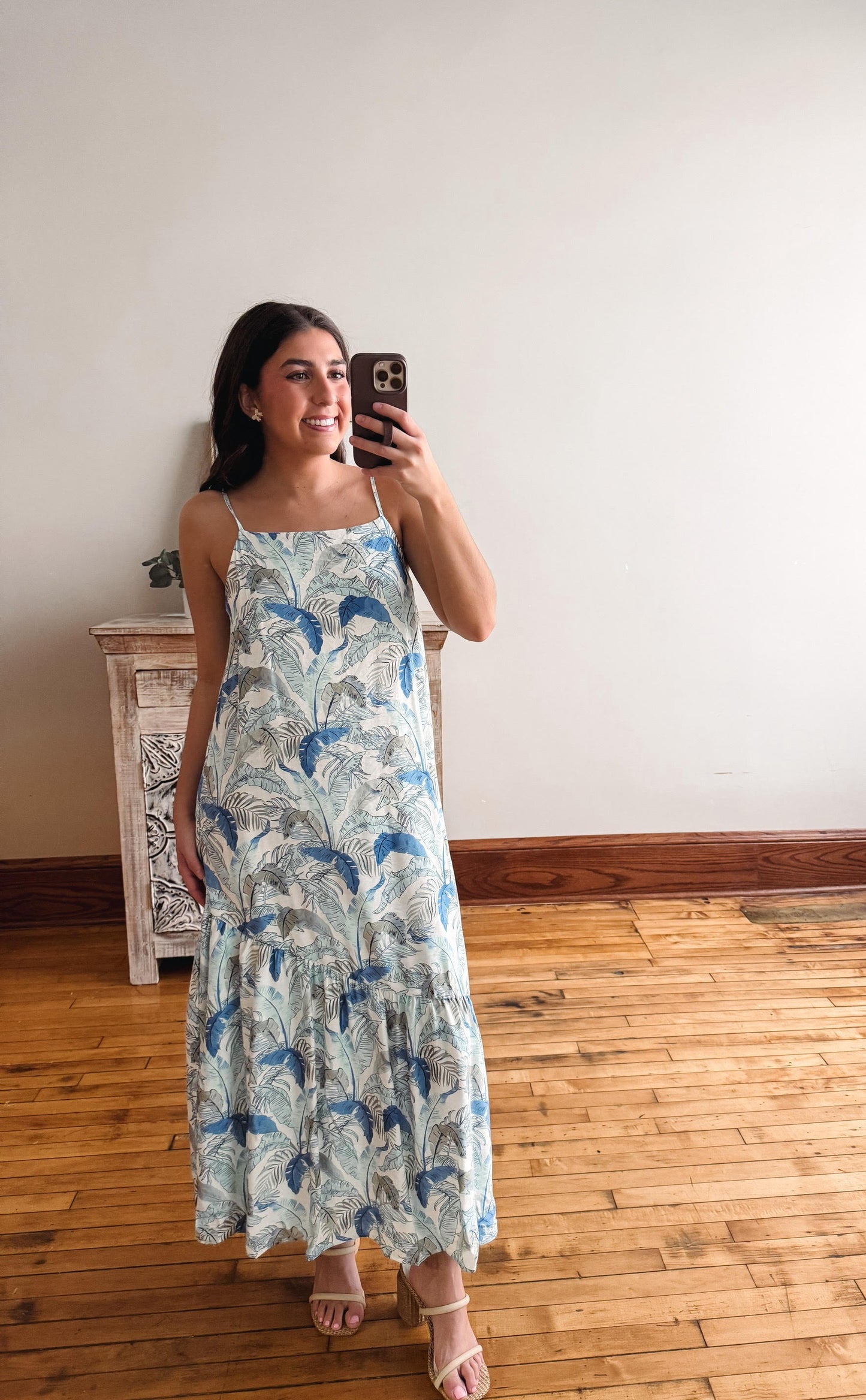 Woman taking a mirror selfie wearing a floral dress in a room with wooden flooring.