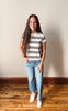 Woman wearing a striped shirt and jeans standing on a wooden floor with a plain wall background