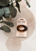 A tortoiseshell flat cloud clip by kitsch on its original cream-colored card packaging, styled on a textured beige surface with a green eucalyptus plant in the background.