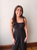 Woman wearing a black jumpsuit standing against a plain wall.