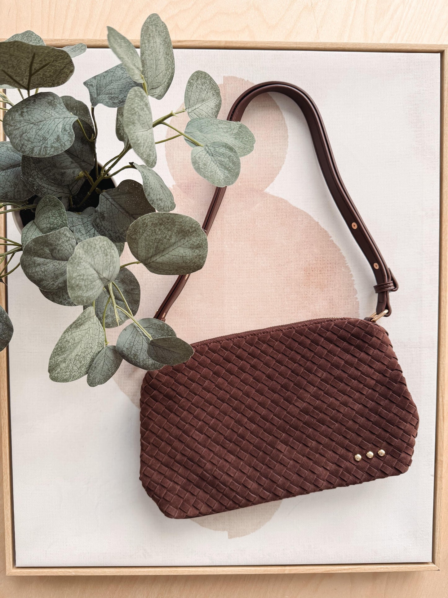 Brown textured handbag with a plant on a light background