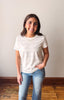 Woman wearing a white striped shirt and blue jeans standing against a plain wall.