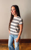 Woman wearing a striped shirt and jeans standing against a plain wall.
