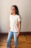 Woman wearing a striped shirt and jeans standing against a plain wall.