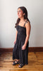 Woman wearing a black dress standing on a wooden floor with a white wall background