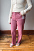 A person wearing a pair of pink denim jeans with a cream ribbed long-sleeve henley top and white slide sandals, standing on a wooden floor against a gray wall.