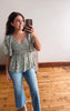 Woman taking a mirror selfie wearing a green floral blouse and blue jeans.