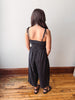 Person wearing a black jumpsuit standing on a wooden floor with a white wall background