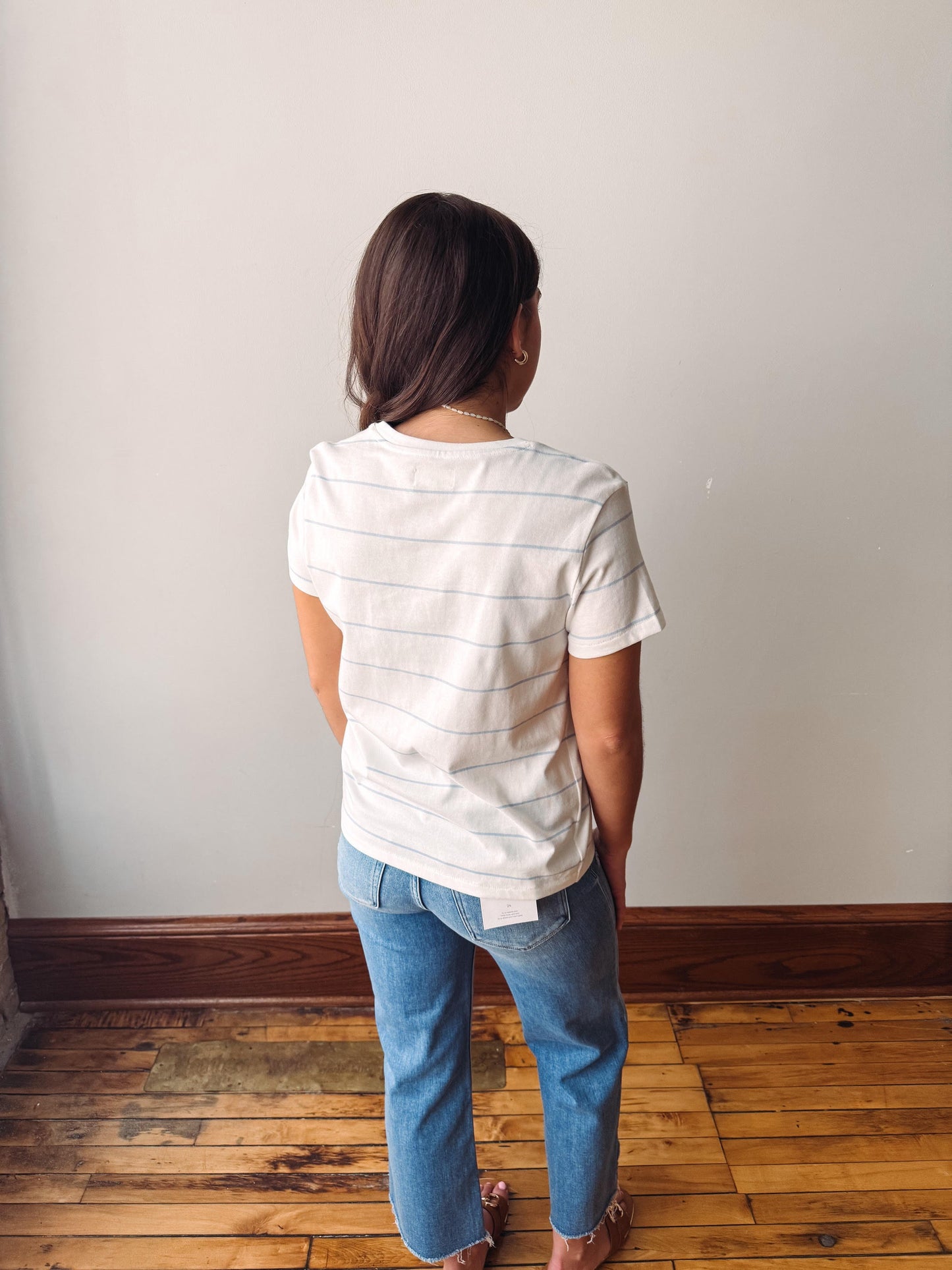 Person wearing a white striped shirt and blue jeans standing against a plain wall.