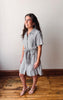 Woman wearing a checkered dress standing on a wooden floor with a white wall background