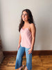 Woman wearing a pink top and blue jeans standing against a plain wall.