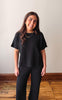 Woman wearing a black t-shirt and black pants standing against a plain wall.