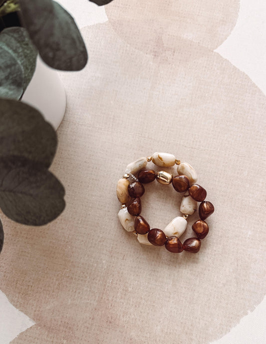 Stack of beaded bracelets on a textured surface with a plant in the background