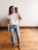 Woman taking a mirror selfie wearing a white t-shirt and blue jeans in a room with wooden flooring.