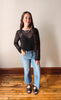 Woman wearing a black mesh top and blue jeans standing on a wooden floor.