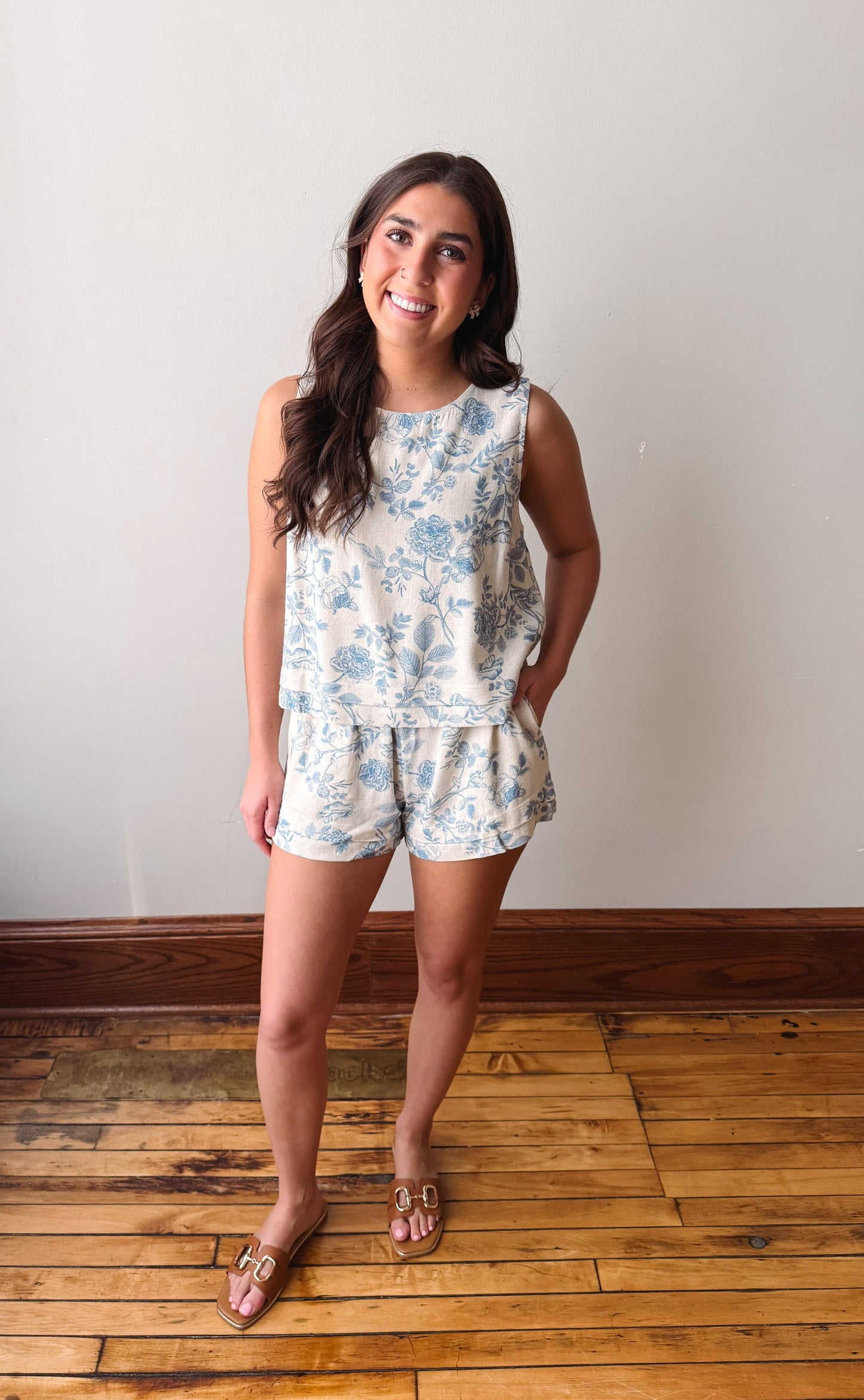 Woman wearing a floral romper standing on a wooden floor with a white wall background