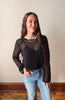 Woman wearing a black mesh top and blue jeans against a plain wall.
